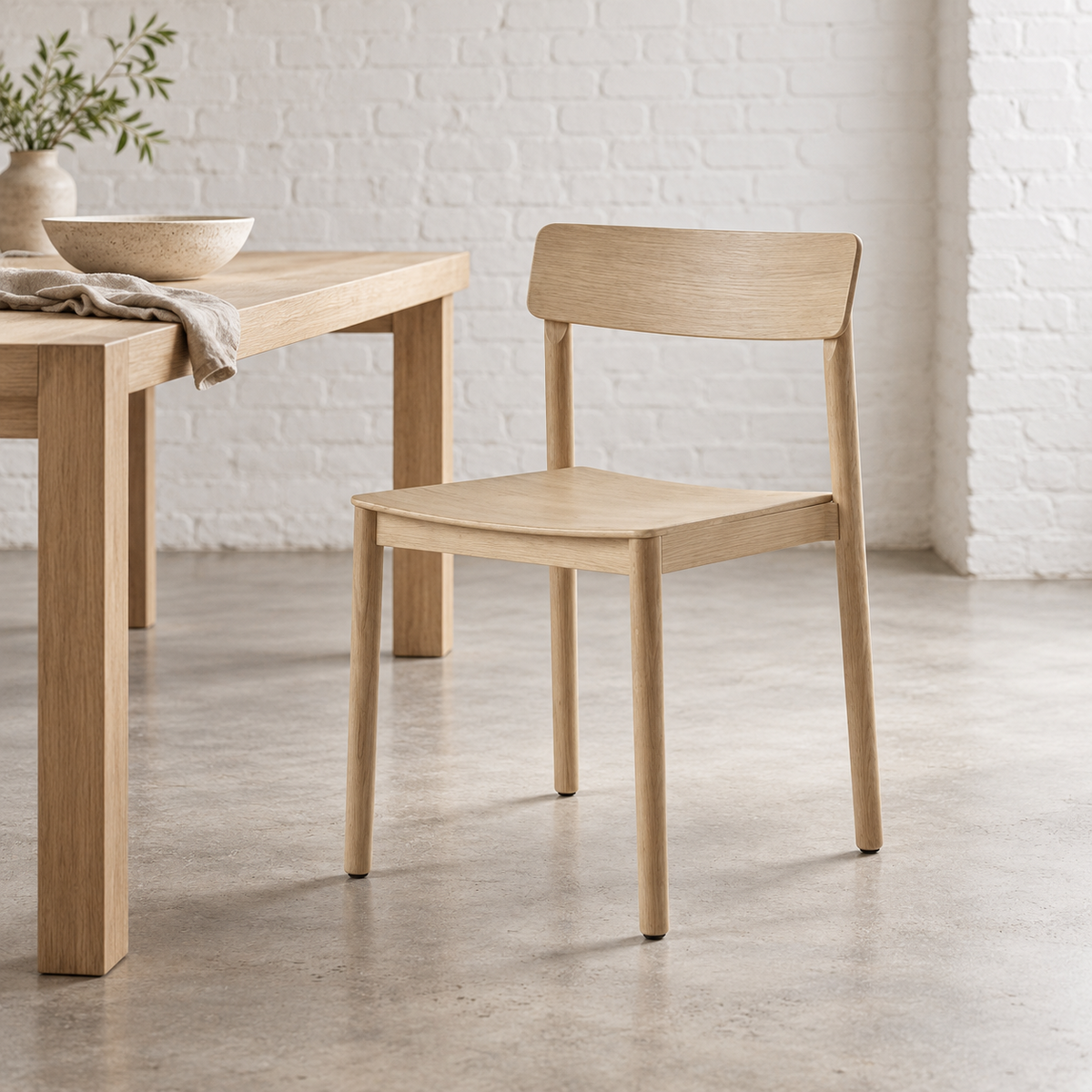 Ori chair in pale wood beside a dining table in a white brick interior